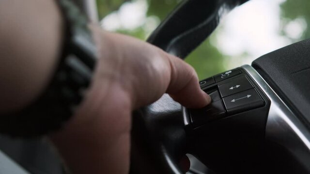 close view of a man hand pressing or push plus button, then minus button on steering wheel of expensive car.