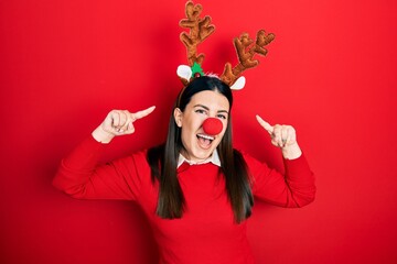 Young hispanic woman wearing deer christmas hat and red nose smiling pointing to head with both hands finger, great idea or thought, good memory