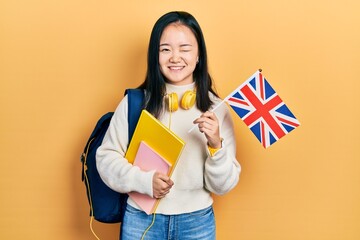 Young chinese girl exchange student holding uk flag winking looking at the camera with sexy...