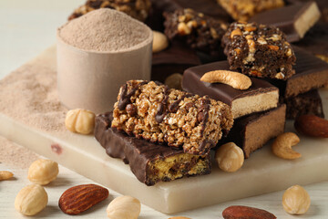 Different tasty energy bars, nuts and protein powder on white table, closeup