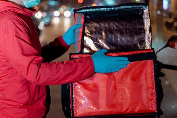 Stock photo of a food deliveryman in red uniform carrying a food delivery box to deliver for customer for order during COVID-19 pandemic and  lockdown in the city at night time in Thailand.