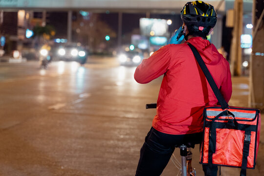 Stock photo of a food deliveryman in red uniform carrying a food delivery box to deliver for customer for order during COVID-19 pandemic and  lockdown in the city at night time in Thailand.