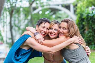 Three happy mature female friends hugging together and looking to camera