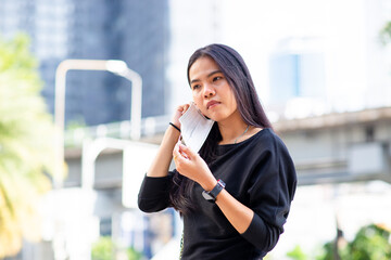 Asian woman be wearing a face mask for protection virus or pollution Hand holding a mask on outdoor city background. coronavirus protect. Sick protect such as Air, Dirt, Fever. Health.