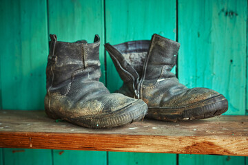 Old dirty torn shoes stand on a wooden shelf against the background of a green wall.