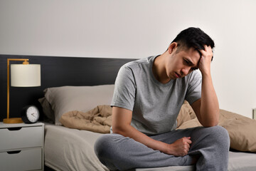 Depressed young Asian man sitting in bed cannot sleep from insomnia