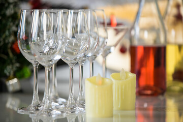Close up shot of white chocolate candles on counter bar in front of empty line of tall wine glasses soft drink beverage alcoholic liquor glass bottles and decoration Xmas tree in blurred background