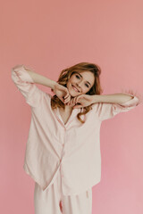 Curly haired woman in pink cute pajamas smiling and looking into camera on isolated background. Girl with blond hair posing..
