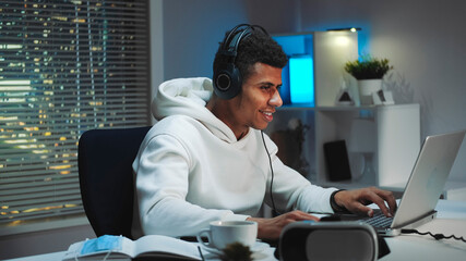 Close-up shot of Black gamer in white hoodie and with headphones playing games on computer in the...