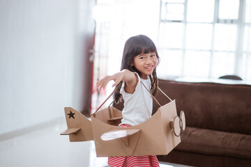 girl playing with cardboard toy airplane at home