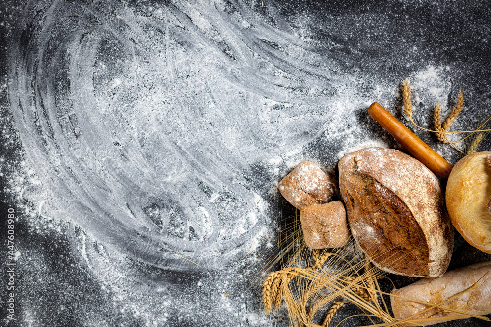 Poster Bakery. Freshly baked crispy bread and buns with ears of wheat on a dark background with copy space top view