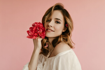 Portrait of curly charming woman with flower in her hair in white blouse posing and holding tulips on isolated pink background..