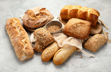 Various types of fresh baked bread on light gray background.