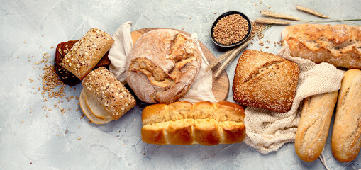 Various types of fresh baked bread on light gray background.