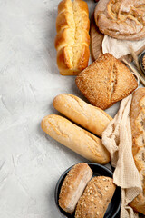 Various types of fresh baked bread on light gray background.