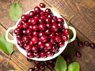 Cherry berries in a green cup on a wooden table top view.