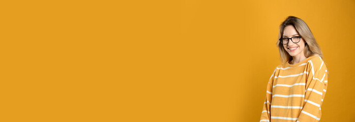 Portrait of happy young woman with beautiful blonde hair and charming smile on yellow background. Space for text