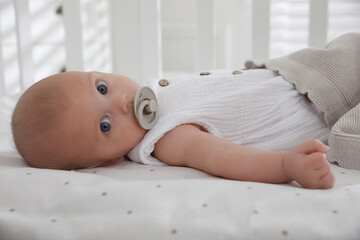Cute little baby with pacifier lying on bed