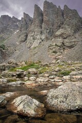Obraz premium View of sky pond in Rocky Mountain National Park in Colorado. Sharp teeth-like peaks can be seen as well as the pond water with rocks and a purple sky.