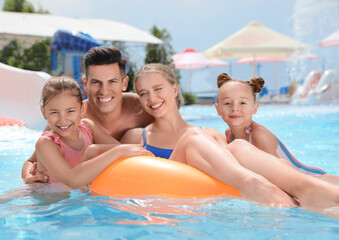 Happy family with inflatable ring in swimming pool at water park