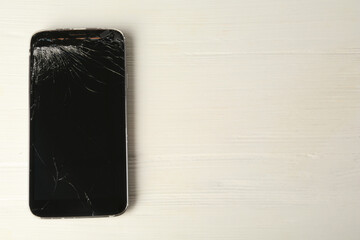 Damaged smartphone on white wooden table, top view with space for text. Device repairing