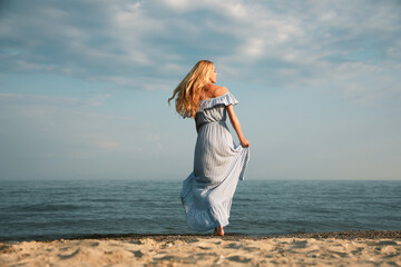 Beautiful young woman on sea beach, back view