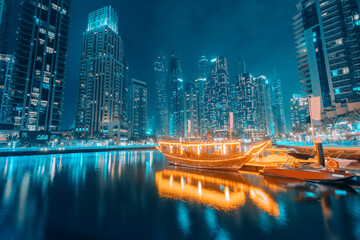 Illuminated by numerous lights, the ferry ship stylized as a traditional Arab boat Abra Dhow sails through the waters of the Dubai Marina - obrazy, fototapety, plakaty