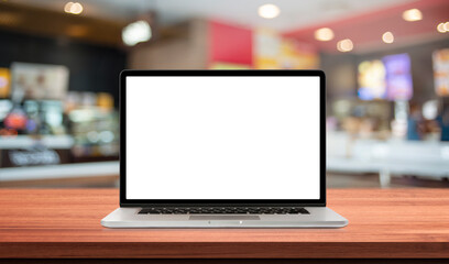 Laptop or notebook with blank screen on wood table in blurry background with fast food restaurant or coffee shop ,nature orange bokeh and sunlight in morning.