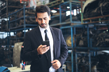 Business owner or Worker or Engineer wear suit work in factory and talk with customer by smartphone, Check stock and inspection in machine spare part engine warehouse