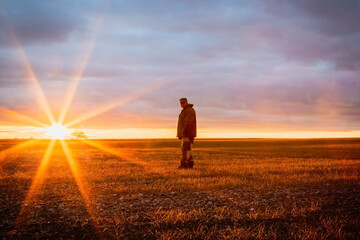 Enchanting sunrise, one male farmer in a field at dawn on the horizon against the backdrop of the rising sun with rays in the early morning
