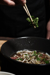 Chef adding greens with chopsticks to pho bo