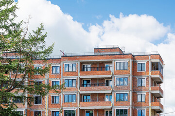 Construction of a multi-storey residential building made of red brick,  illuminated by the evening sun against the blue sky with clouds