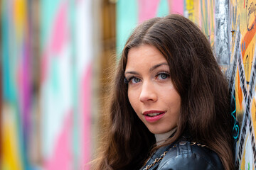 pretty young city girl standing against an exterior wall sprayed with graffiti and looking at the camera