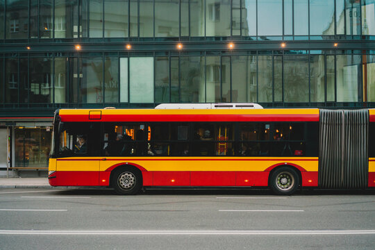 A yellow and red articulated bus parked near business center in the city. Bendy. Tandem. Vestibule bus. Stretch bus. An accordion bus. Articulated vehicle used in public transportation