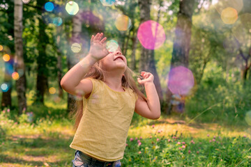happy caucasian child girl in a yellow t-shirt catches a lot of soap bubbles on a summer day. outdoor activity, rainbow, blur