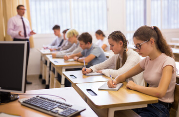 Fototapeta premium Smart teenagers studying in classroom, listening to lecturer and writing in notebooks
