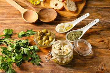 Glass jar with tasty feta cheese, oil, olives and spices on wooden background