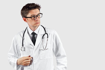 Fototapeta premium Doctor with a stethoscope on a white background. A man in a medical gown with glasses. A doctor with a pensive expression on his face.