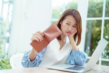 Obraz premium Half-body portrait of an Asian woman in a white shirt sitting in a bakery examining her purse for money with a stressed, unhappy face.