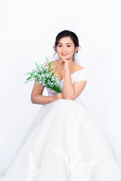 Asian middle-aged woman wearing a bride's dress holding a white flower sitting on a chair behind white background