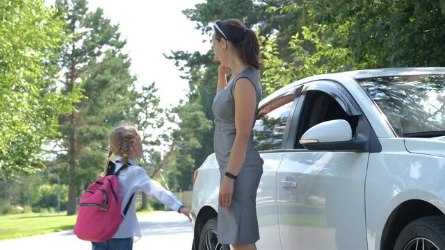Young Mother Putting Schoolbag on Daughter near Car, Saying Goodbye to her Child near School
