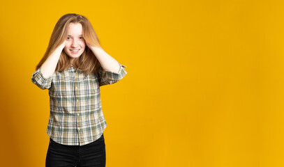 Banner copy space. Pretty young girl, with long hair, laughs, shows a beautiful smile, dressed in a plaid shirt, on a yellow background.
