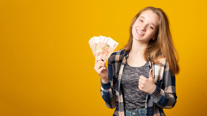 Banner copy space. Happy young woman holding Russian rubles, wearing a plaid shirt, received a scholarship, a salary on a yellow background. Finance concept.