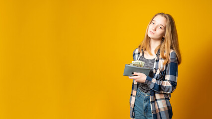 Banner copy space. Cute young girl with gray wallet full of money dollars on a yellow background.