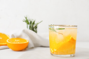 Glass of tasty orange cocktail with rosemary on light background