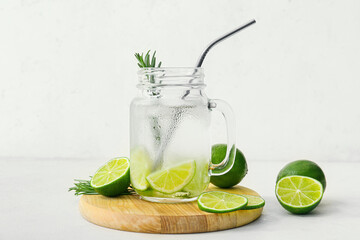 Mason jar of tasty lime cocktail with rosemary on light background