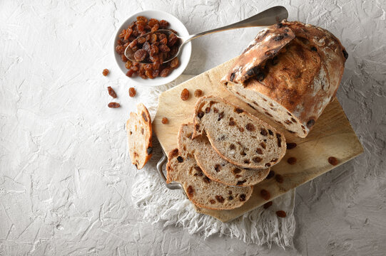 Raisin bread, traditional loaf of sliced bread with cutting board and rustic white plaster background, closeup. Top view, space for text.