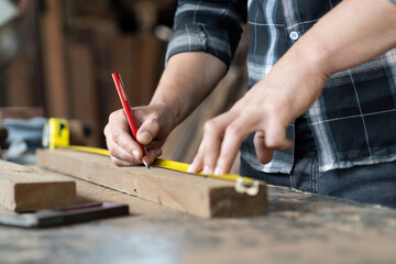 Male carpenter using pencil drawing sign on plank. Craftsman doing his job at the carpentry workshop