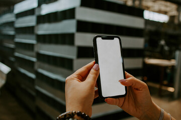 A hand holds a white mobile phone with an empty white screen on the background of the factory