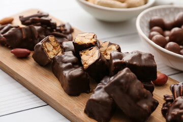 Board with tasty chocolate candies on light wooden background, closeup